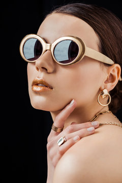 young naked woman in sunglasses and golden jewelry isolated on black