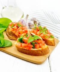 Bruschetta with tomato and spinach on light wooden table