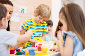 Children with teacher play colorful clay toy in daycare