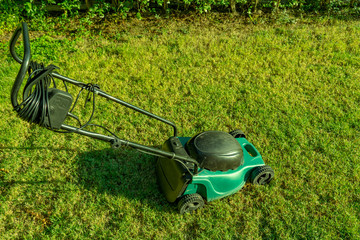 Four wheels electric lawn mower on short green grass lawn on sunny day with evening yellow sunlight.