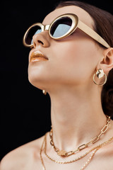 young attractive naked woman in sunglasses and golden jewelry isolated on black