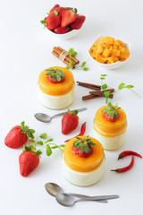 Traditional Italian sweet dessert Panna cotta with mango jelly with touch of red hot chili Piri-Piri served in jars on white wooden table and embellished with fresh real strawberrries and mint.