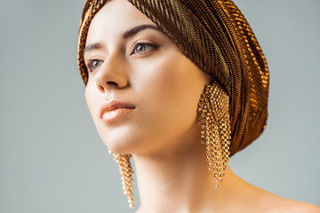 young naked woman with shiny makeup, golden rings in turban looking away isolated on grey - obrazy, fototapety, plakaty