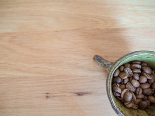 Close up roasted coffee beans in a ceramic cup on wood table.