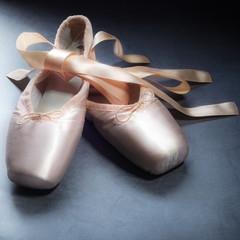 Pointe shoes ballet dance shoes with a bow of ribbons beautifully folded on a dark background.
