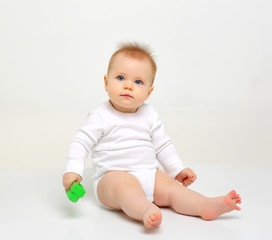 Fototapeta premium Charming blue-eyed baby sitting on a white background with colored educational toys