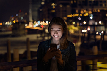 young woman using her smartphone during the night. city light as background