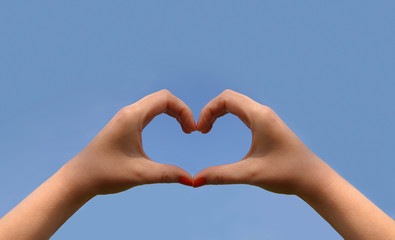 A woman's hands are held high towards a blue sky. She places her hands and fingers to create a...