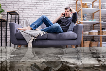 Man Sitting On Sofa Calling To Plumber