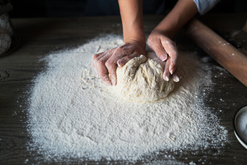 Dough for bread or pizza on a wooden surface with natural light. Hands cooking dough on dark wooden background. Food concept. Selective focus.