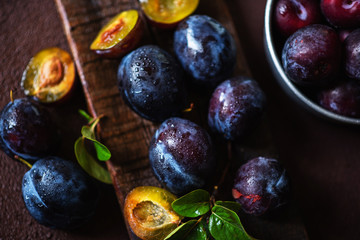 Garden plums on table. Close up of fresh plums with leaves. Summer or autumn harvest of plums. Toned image. Selective focus.