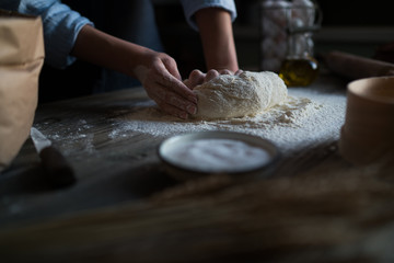 Baking concept. Working woman prepares pastry by himself, kneads dough on wooden counter with flour and rolling pin. Female cook bakes bread or delicious bun.