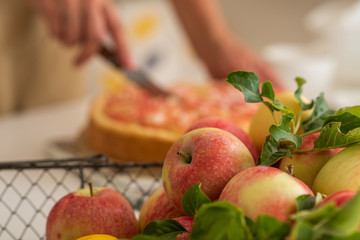 Ripe organic apples in vintage basket on rustic white table. Apple cheesecake in the background. Summer homemade apple tart with ingredients. Healthy organic food. Tasty breakfast.
