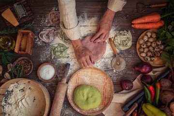 Senior woman cook making tagliatelle pasta with dough in restaurant kitchen. Making pasta. Making pasta in restaurant. Colored raw vegetable pasta with beets, carrots and spinach.