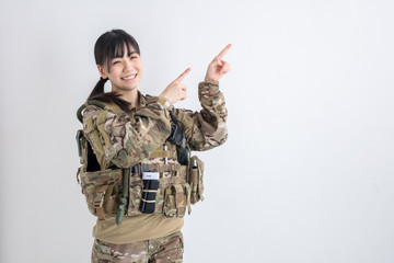 白背景に迷彩服の女の子が笑顔で両手で指を指しているサバイバルゲーム
