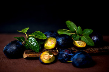 Plums in drops on dark wooden background. Half and whole of blue plum fruit. Many beautiful plums with leaves. Toned image. Selective focus.