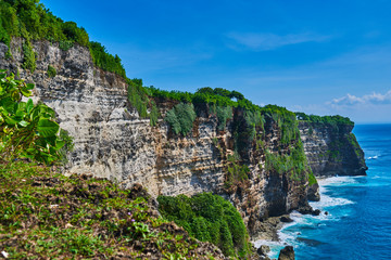 Azure beach with rocky mountains and clear water with huge waves of Indian ocean at sunny day. View of Uluwatu cliff and blue sea in Bali, Indonesia. Beautiful world, travel, holiday.