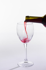 Red wine pouring from bottle into big glass on white background