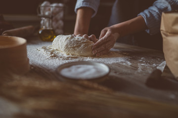 Woman kneading dough for pasta or pizza on table. Dough, flour with kitchen utensils on the old wooden table. Healthy, organic and vegetarian food. Food concept. Selective focus. Rustic style.