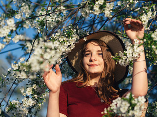Fashion spring portrait of a woman in a blooming garden. Happy woman in hat