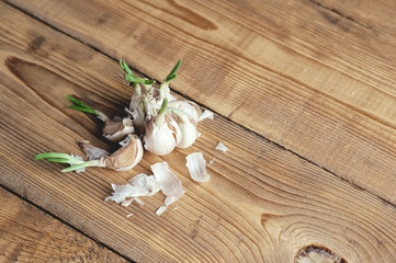 Garlic bulbs on wooden background. The harm of garlic to human health. Broken garlic cloves with husks are scattered on the surface of the cutting board.
