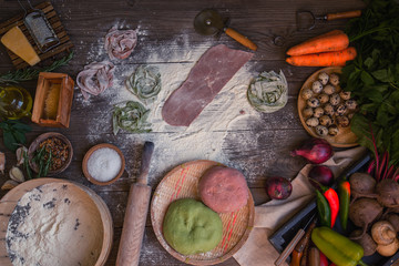 Fresh homemade pasta with pasta ingredients on the dark wooden table top view. Italian pasta tagliatelle on a dark wooden table. Colored raw vegetable pasta with beets, carrots and spinach.