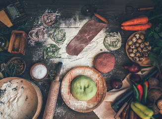 Fresh homemade pasta with pasta ingredients on the dark wooden table top view. Italian pasta tagliatelle on a dark wooden table. Colored raw vegetable pasta with beets, carrots and spinach.