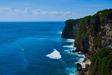 Azure beach with rocky mountains and clear water with huge waves of Indian ocean at sunny day. View of Uluwatu cliff and blue sea in Bali, Indonesia. Beautiful world, travel, holiday.