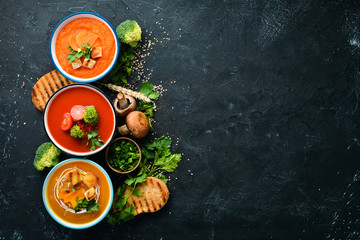 Assortment of colored vegetable cream soups. Dietary food. On a black stone background. Top view....