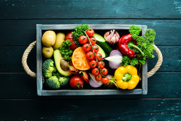 Fresh vegetables and fruits in a wooden box. Avocados, tomatoes, strawberries, melons, potatoes, paprika, citrus. Top view. Free space for your text.