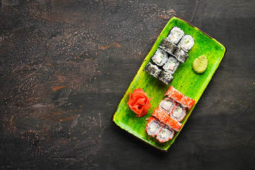 Variation of sushi and rolls on a plate. Top view. Free space for your text. On a dark background.