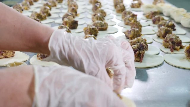 Closeup shot of meat dumplings hand making. Sculpt meat balls. Female workers in white latex gloves and uniform wrap meat in dough. Meat factory proccesing. 4k