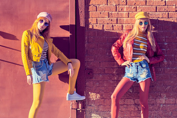 Two Girl Having Fun on Street. Outdoor Fashion. Carefree Woman posing near Brick Wall. Happy positive emotion. Pop Art. Stylish Hipster Friends in Creative Colorful Outfit, Sunglasses, funny concept