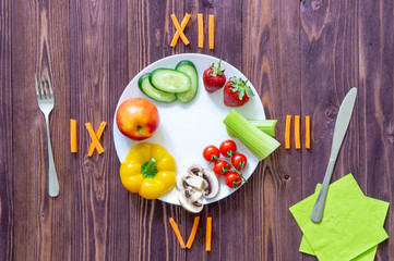 food clock with Roman numerals. white plate knife and fork, vegetables, strawberries, two eggs,...