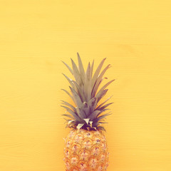 Ripe pineapple over yellow wooden background. Beach and tropical theme. Top view