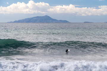 The surfer takes a wave, on a surfboard, slides along the wave, in the background of the mountain, Sorrento Italy