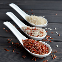Different types of rice in spoons on wooden table background