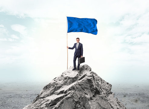 Handsome businessman on the top of the mountain with blue flag
