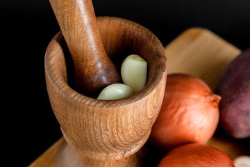 Wooden mortar (pounder), pestle, onion, garlic and other vegetables isolated on black