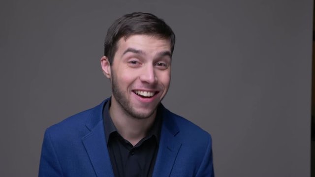 Closeup shoot of young handsome caucasian man dabbing with confidence looking at camera with background isolated on gray
