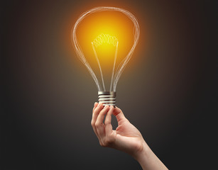 Hand holding light bulb on dark background. New idea concept