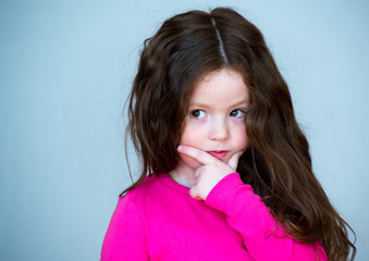 Beautiful girl 4-5 years old with long brown hair. The child is puzzled. In thought.