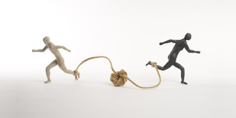 White and black men run with a rope tied to the foot. Concept of the absurd competition. Isolated...