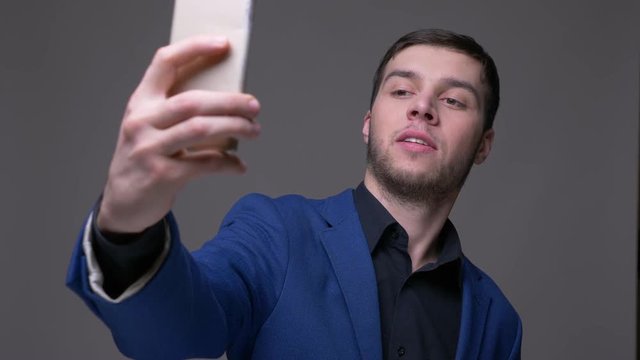 Closeup shoot of young handsome caucasian man taking selfies on the phone with background isolated on gray