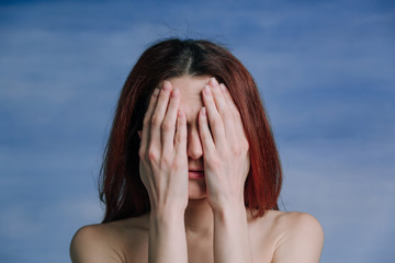 A  woman  covered her face with her hands, on blue background.