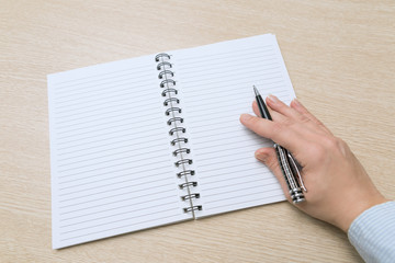 Top view of the table where there is a clean notebook. Women's hand hold a pen and prepare to write something.