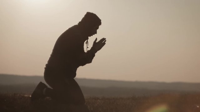 Silhouette young man praying outside at beautiful sunset. Male asks for help finding solace in faith, concept religion.