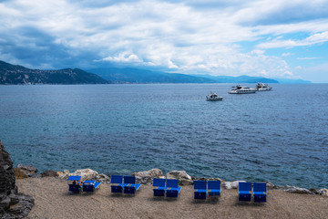 Beautiful view of a private beach on the Ligurian coast. Luxury yachts anchored in the azure sea. Coastline in a blue haze with a beautiful cloudy sky. Travel and luxury vacation on Italian Riviera.