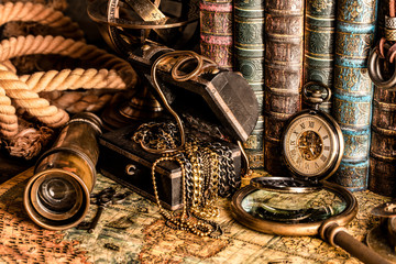 Fototapeta na wymiar Antique clock on the background of a magnifying glass, treasure chest with gold and books. Vintage style. 1565 old map of the year.