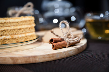 Honey cake lies on a saucer. Green tea in a cup and teapot. Cinnamon is on the board.